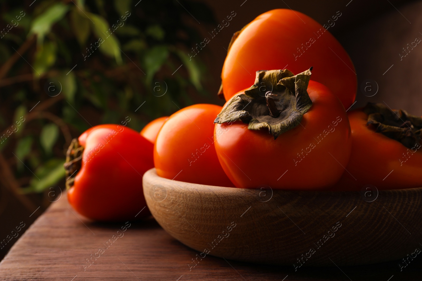 Photo of Delicious ripe persimmons in bowl on wooden table, space for text