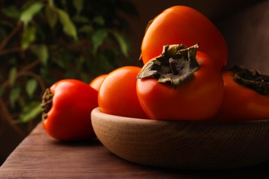 Delicious ripe persimmons in bowl on wooden table, space for text