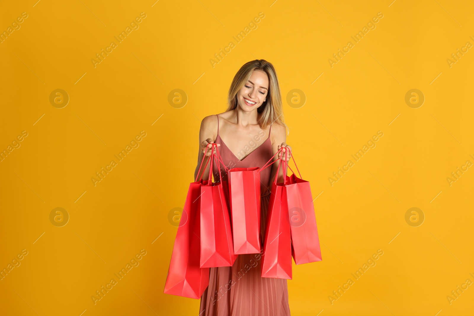 Photo of Happy young woman with shopping bags on yellow background. Black Friday Sale