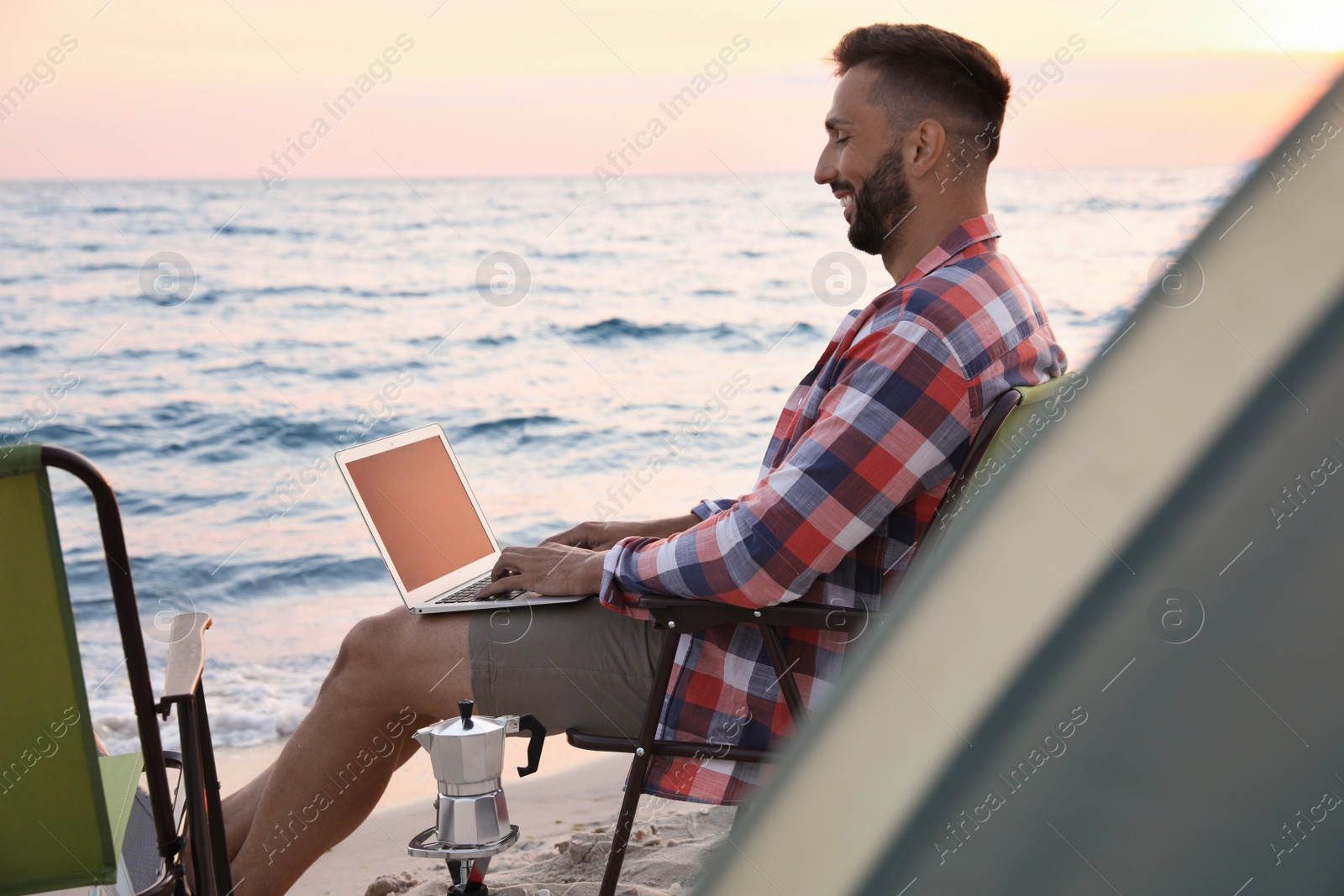 Photo of Man using laptop in camping chair on sandy beach