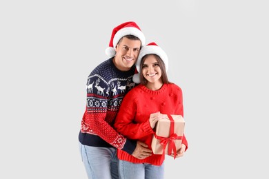 Photo of Beautiful happy couple in Santa hats holding Christmas gift on light background