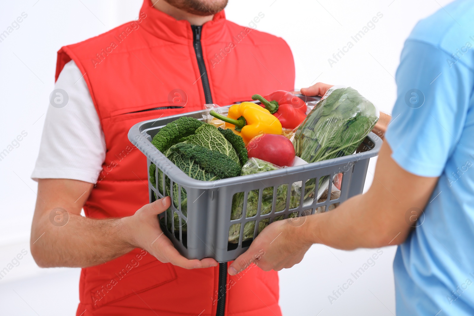 Photo of Courier giving plastic crate with products to customer at home, closeup. Food delivery service