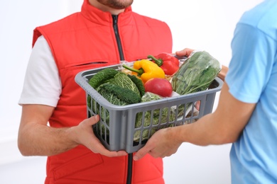 Photo of Courier giving plastic crate with products to customer at home, closeup. Food delivery service