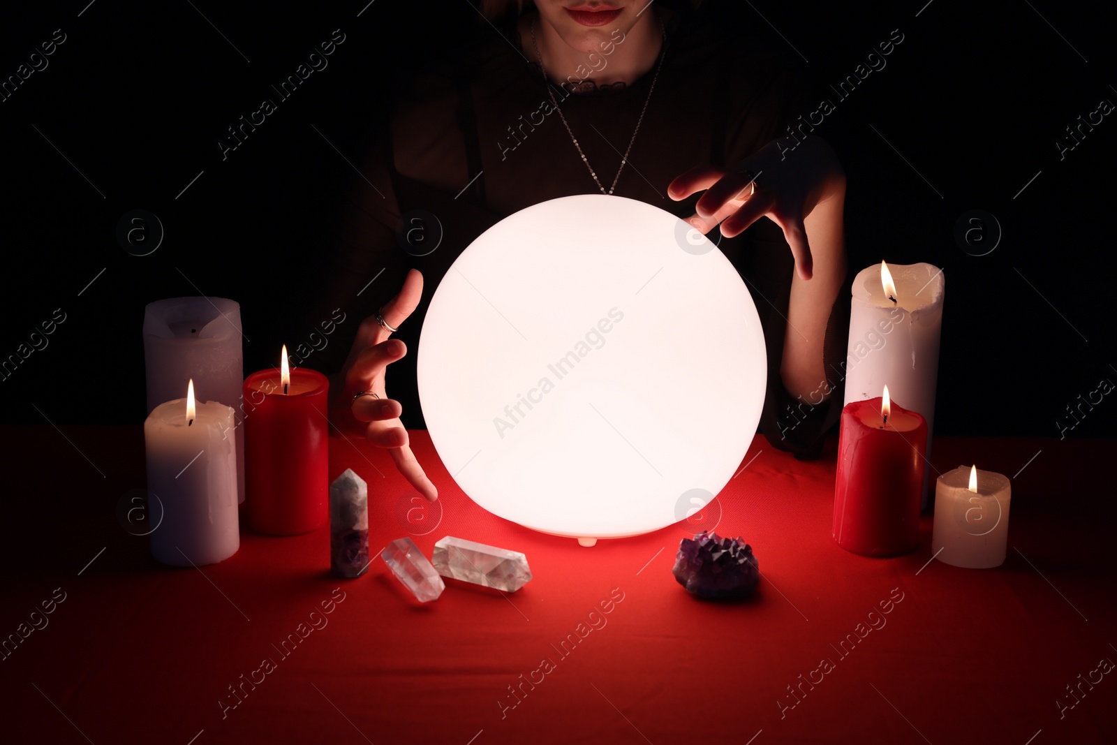 Photo of Soothsayer using glowing crystal ball to predict future  at table in darkness, closeup. Fortune telling