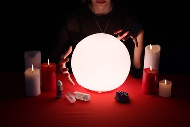 Photo of Soothsayer using glowing crystal ball to predict future  at table in darkness, closeup. Fortune telling