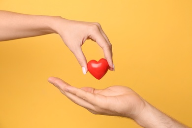 Photo of Woman giving red heart to man on yellow background, closeup. Donation concept