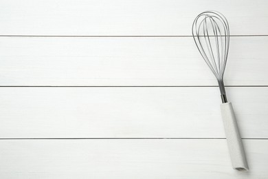 Metal whisk on white wooden table, top view. Space for text