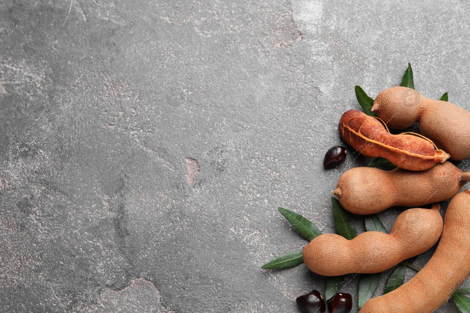 Photo of Ripe tamarinds and fresh leaves on grey table, flat lay. Space for text