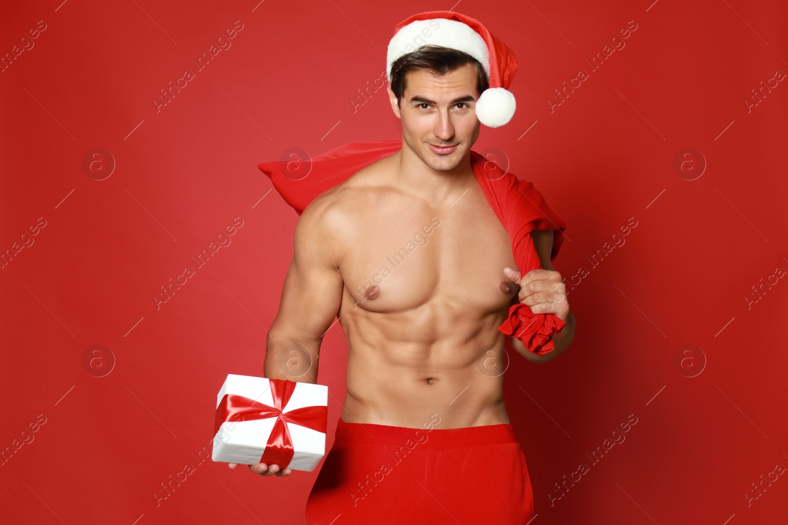 Photo of Sexy shirtless Santa Claus with gift on red background