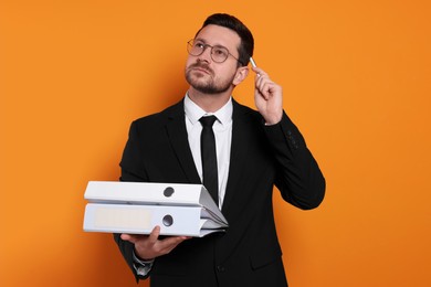 Photo of Thoughtful accountant with folders on orange background