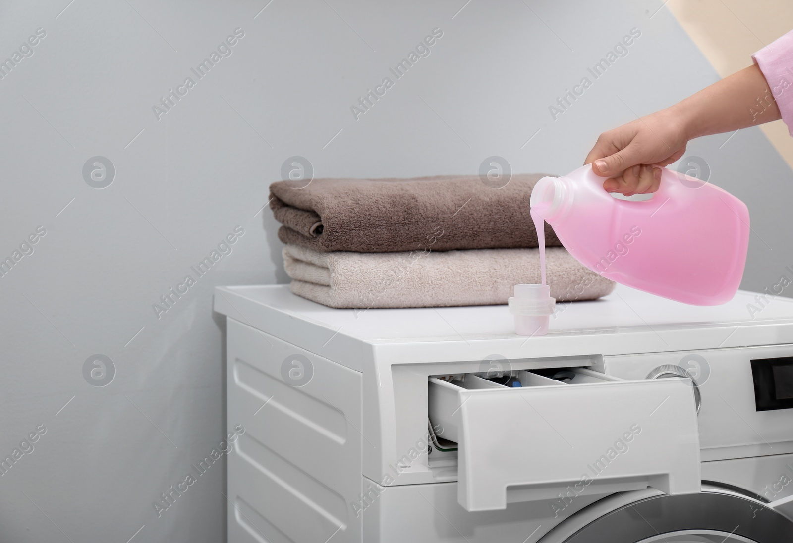 Photo of Woman pouring laundry detergent into cap on washing machine indoors, closeup. Space for text