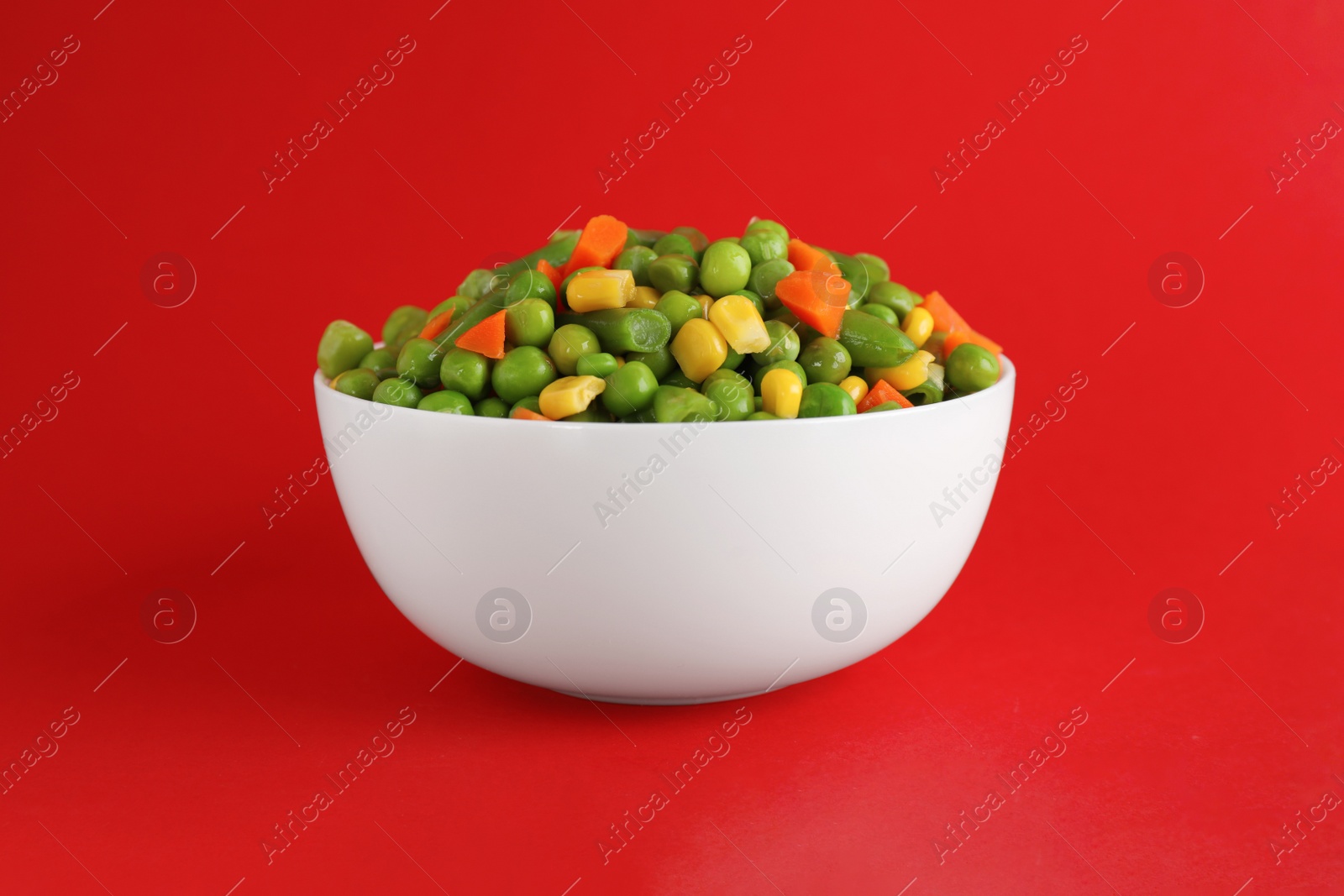 Photo of Mix of fresh vegetables in bowl on red background