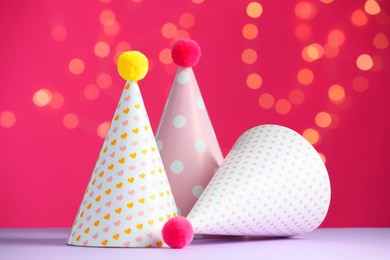 Photo of Party hats on violet table against pink background with blurred lights