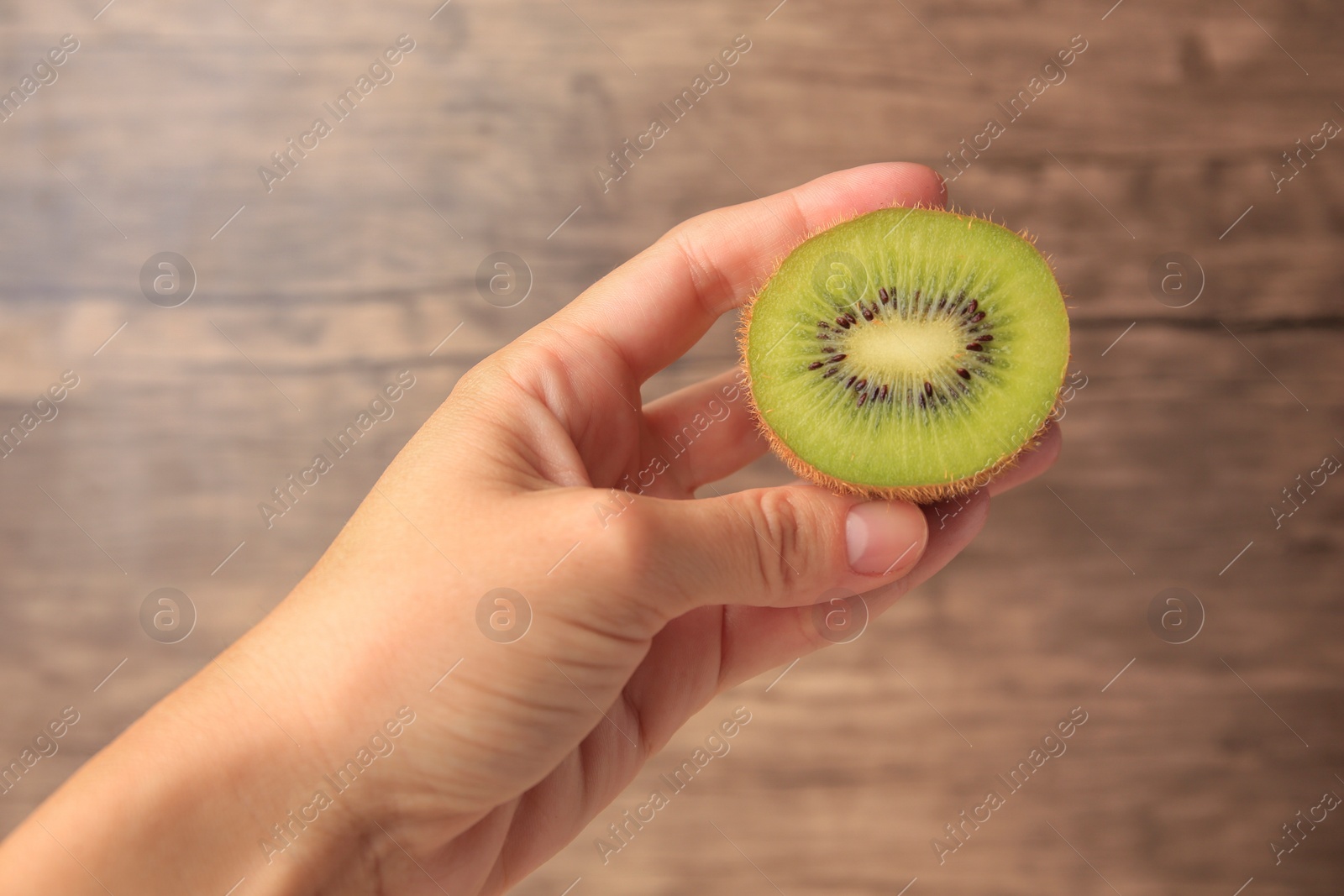 Photo of Woman holding delicious fresh kiwi on wooden background, closeup