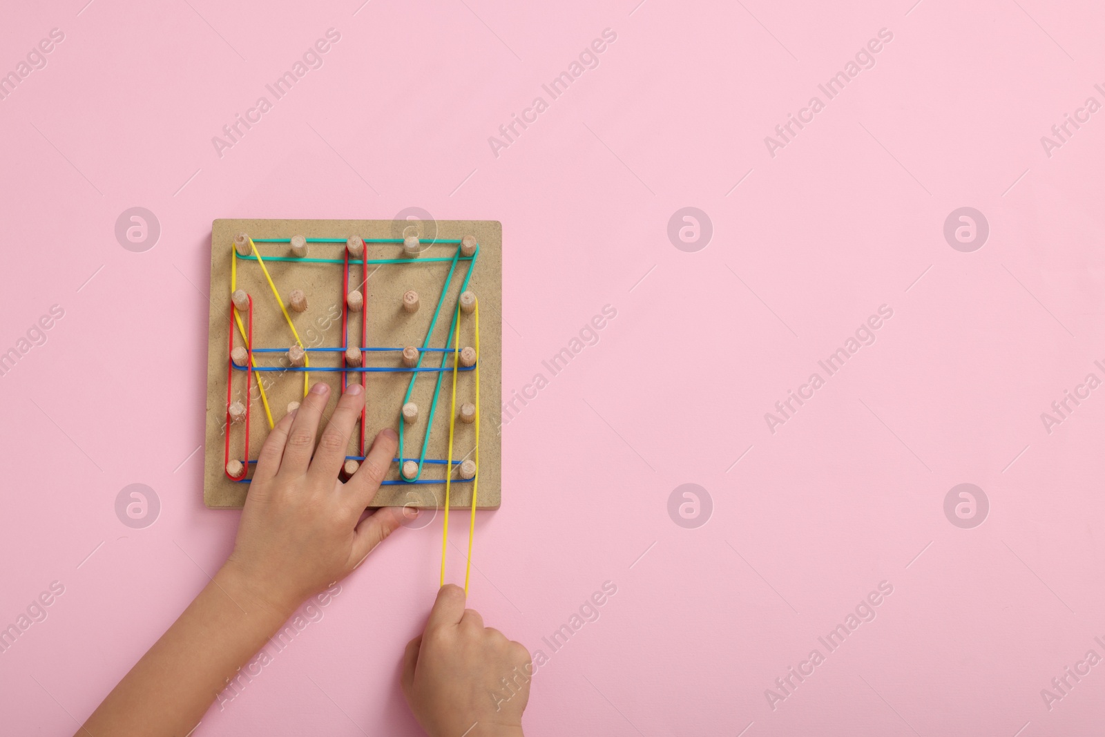 Photo of Motor skills development. Boy playing with geoboard and rubber bands at pink table, top view. Space for text