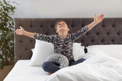 Cute boy with toy stretching after sleep on bed