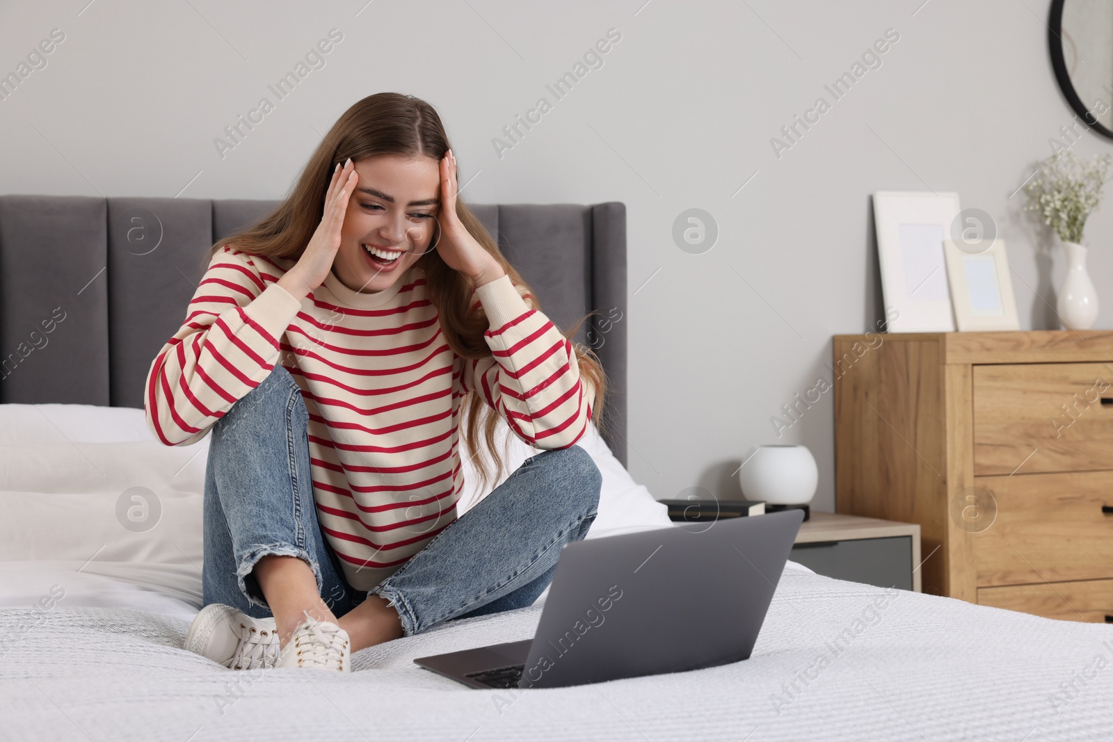 Photo of Surprised woman with laptop on bed in bedroom