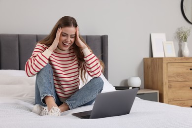 Photo of Surprised woman with laptop on bed in bedroom