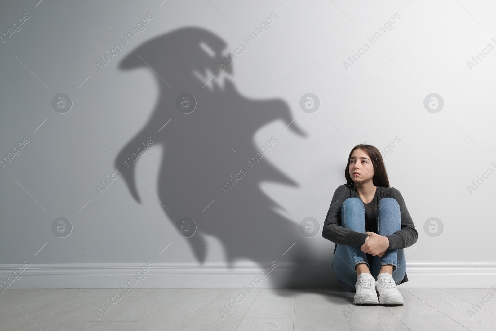 Image of Upset teenage girl suffering from sciophobia and phantom behind her. Irrational fear of shadows