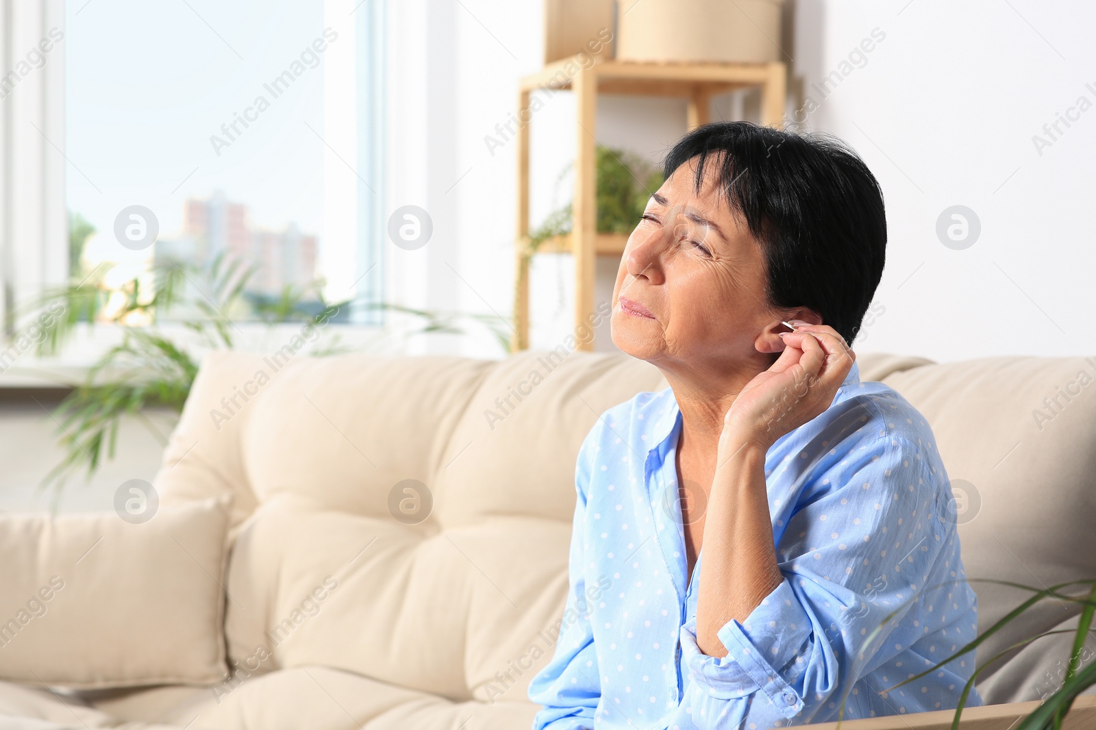 Photo of Senior woman cleaning ear with cotton swab at home. Space for text