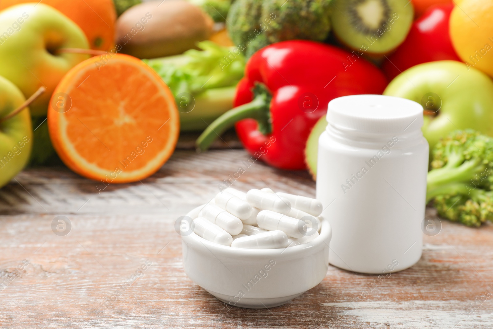 Photo of Dietary supplements. Plastic bottle, pills and food products on wooden table, space for text