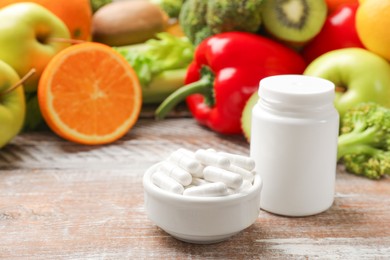 Photo of Dietary supplements. Plastic bottle, pills and food products on wooden table, space for text