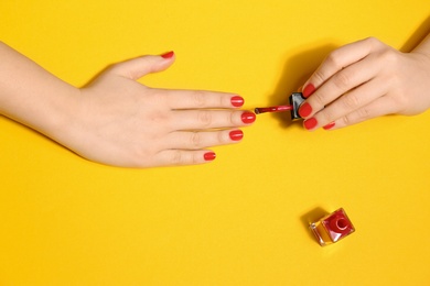 Photo of Woman applying nail polish on color background, top view