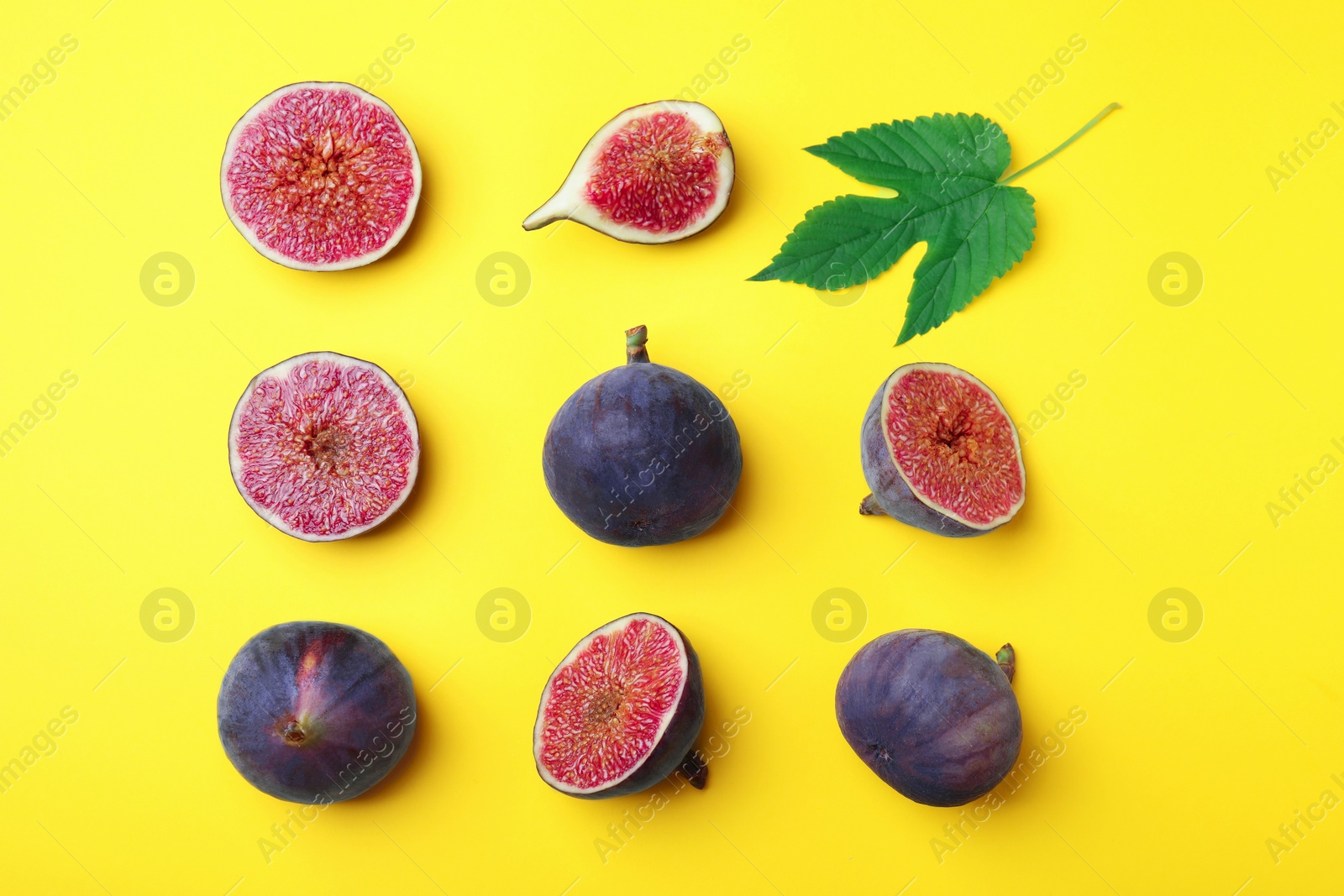 Photo of Fresh ripe figs with green leaf on yellow background, flat lay