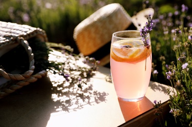 Photo of Glass of fresh lemonade on wooden tray in lavender field
