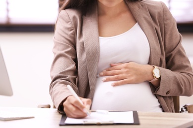 Photo of Young pregnant woman working at desk in office, closeup