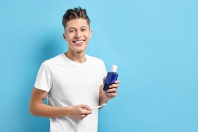 Young man with mouthwash and toothbrush on light blue background, space for text