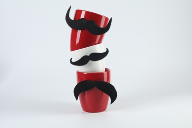 Photo of Cups with fake mustaches on light background