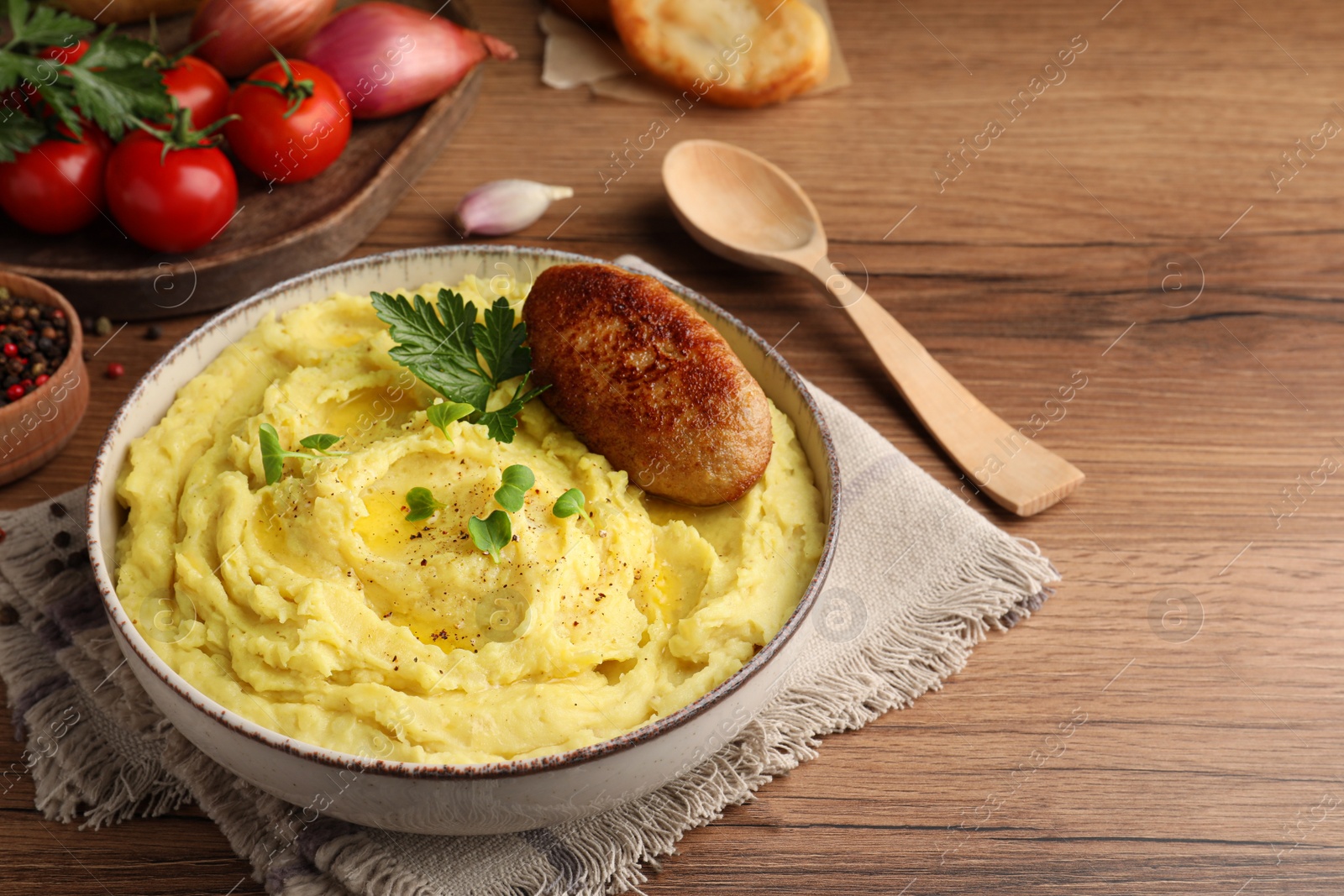 Photo of Bowl of tasty mashed potatoes with parsley, black pepper and cutlet served on wooden table. Space for text