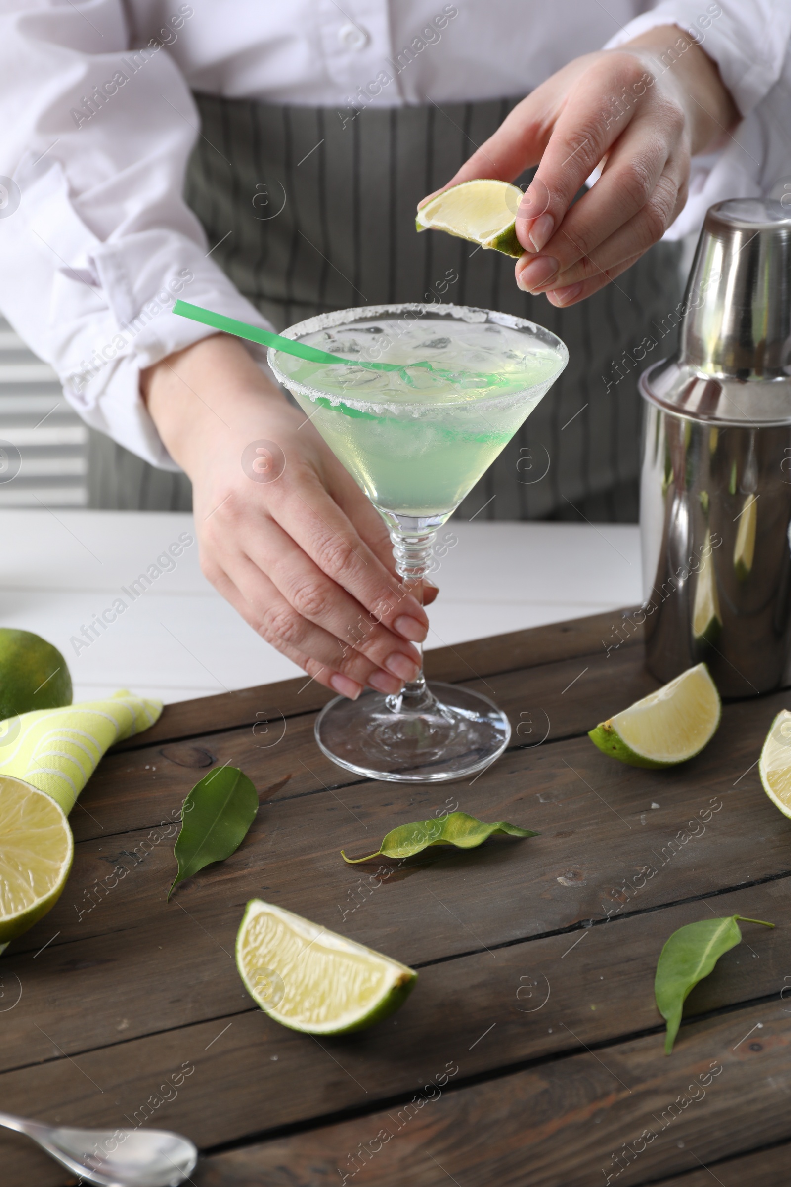 Photo of Bartender squeezing lime juice into glass with delicious Margarita cocktail at wooden table, closeup