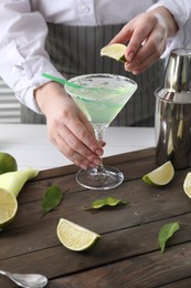 Bartender squeezing lime juice into glass with delicious Margarita cocktail at wooden table, closeup