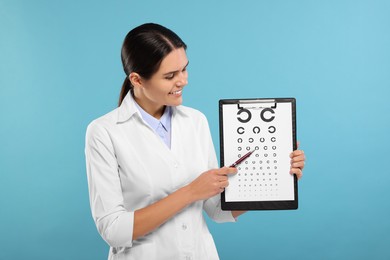 Ophthalmologist pointing at vision test chart on light blue background