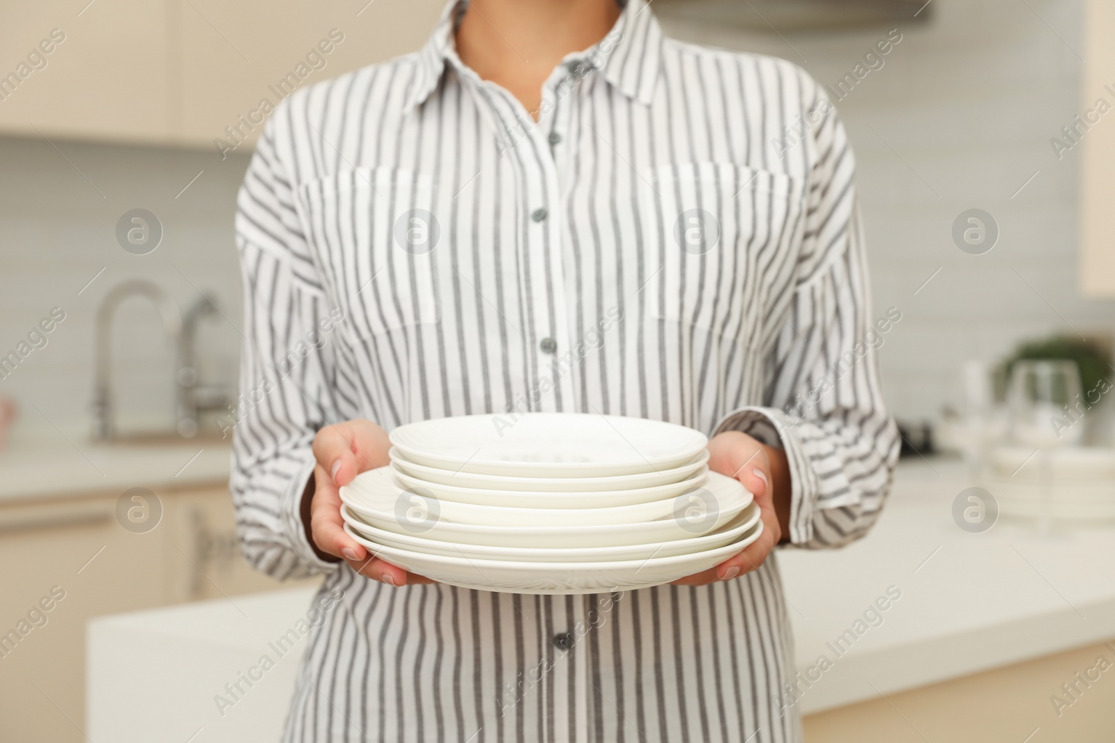 Photo of Woman holding stack of clean dishes in kitchen, closeup