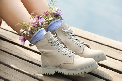 Photo of Woman sitting on wooden pier with flowers in socks outdoors, closeup