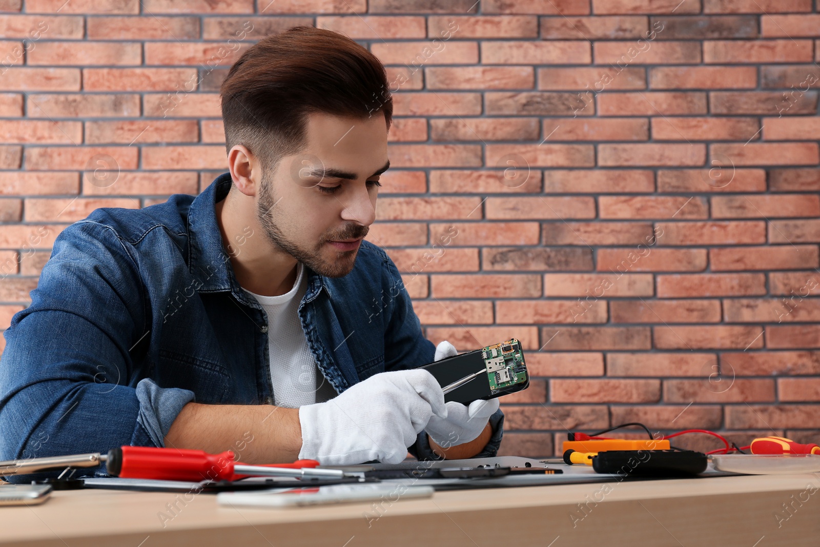 Photo of Technician repairing broken smartphone at table in workshop. Space for text