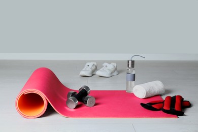 Photo of Exercise mat and other sport equipment on light wooden floor indoors