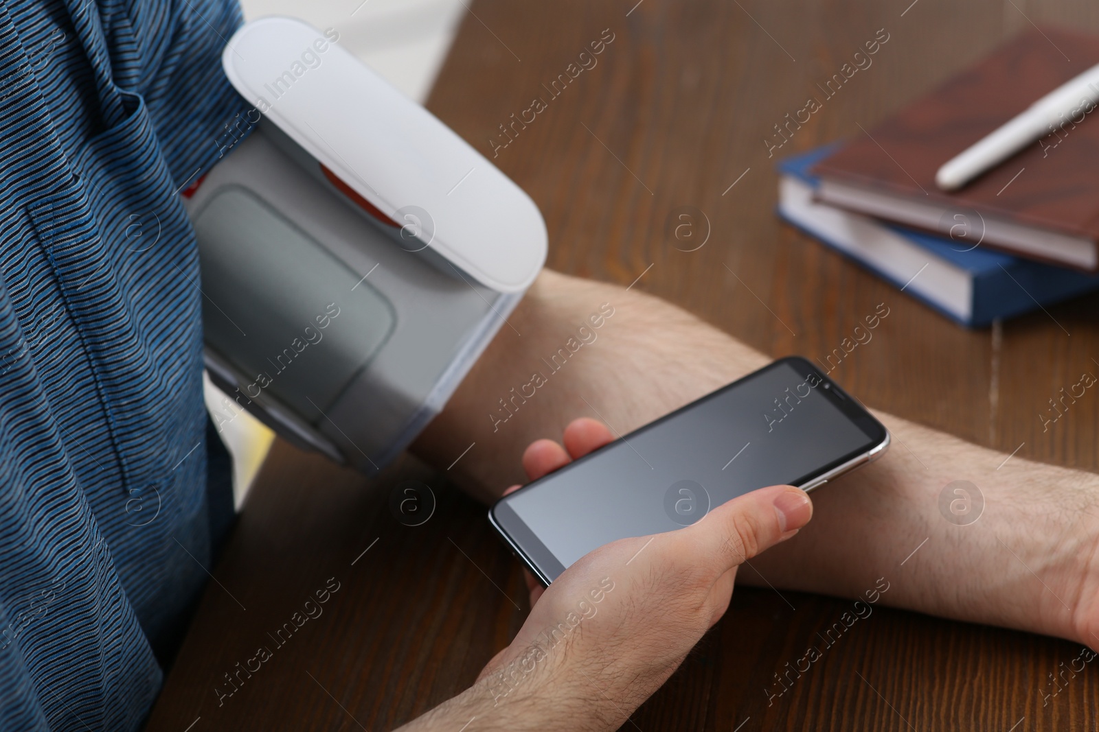 Photo of Man checking blood pressure with modern monitor and smartphone at table indoors, closeup