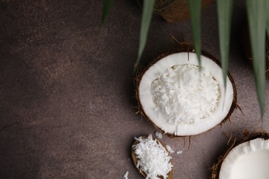 Coconut flakes in nut shell and spoon on brown table, flat lay. Space for text