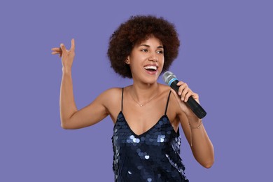 Curly young woman with microphone singing on purple background