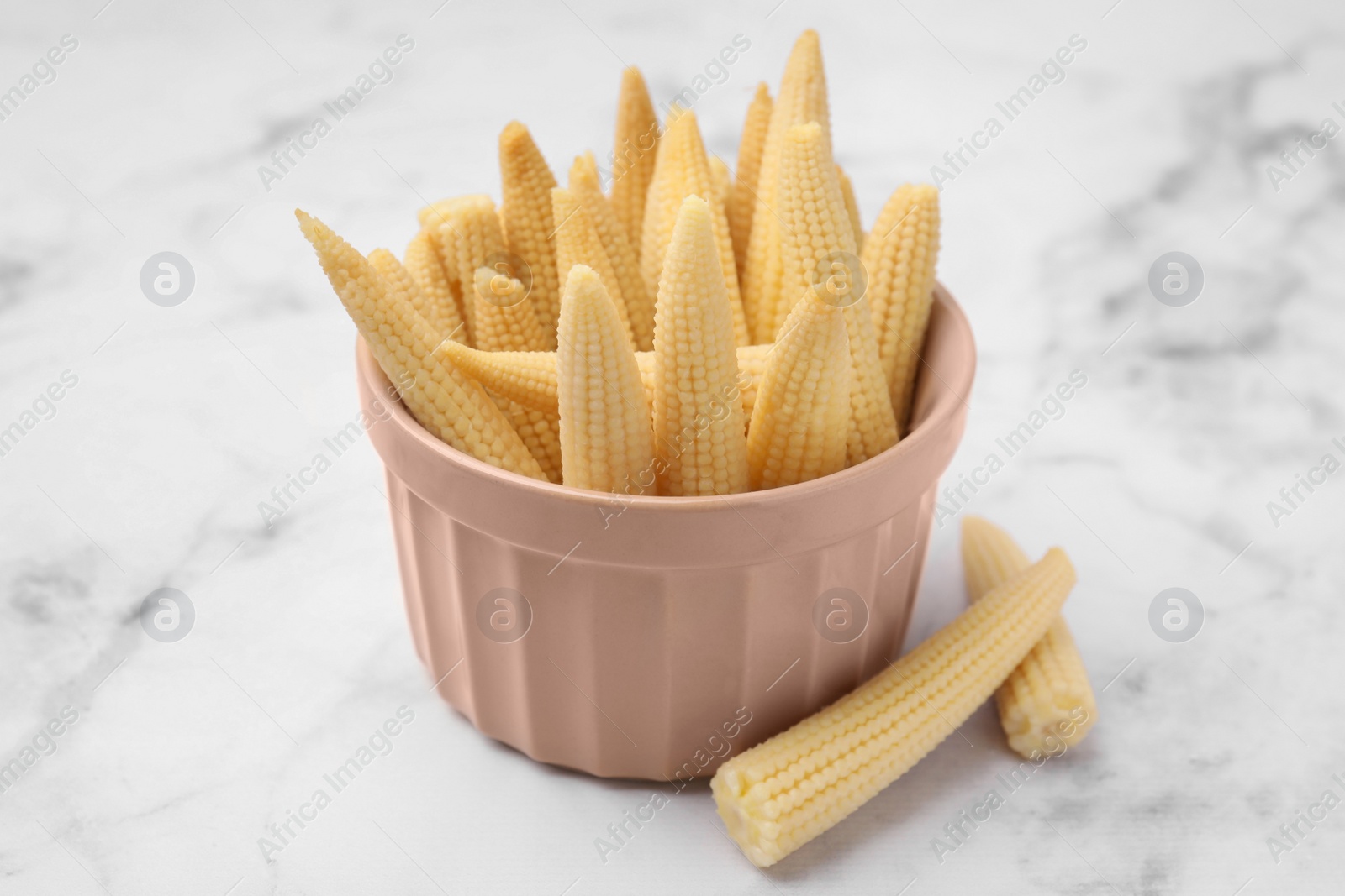 Photo of Bowl and pickled baby corn on white marble table