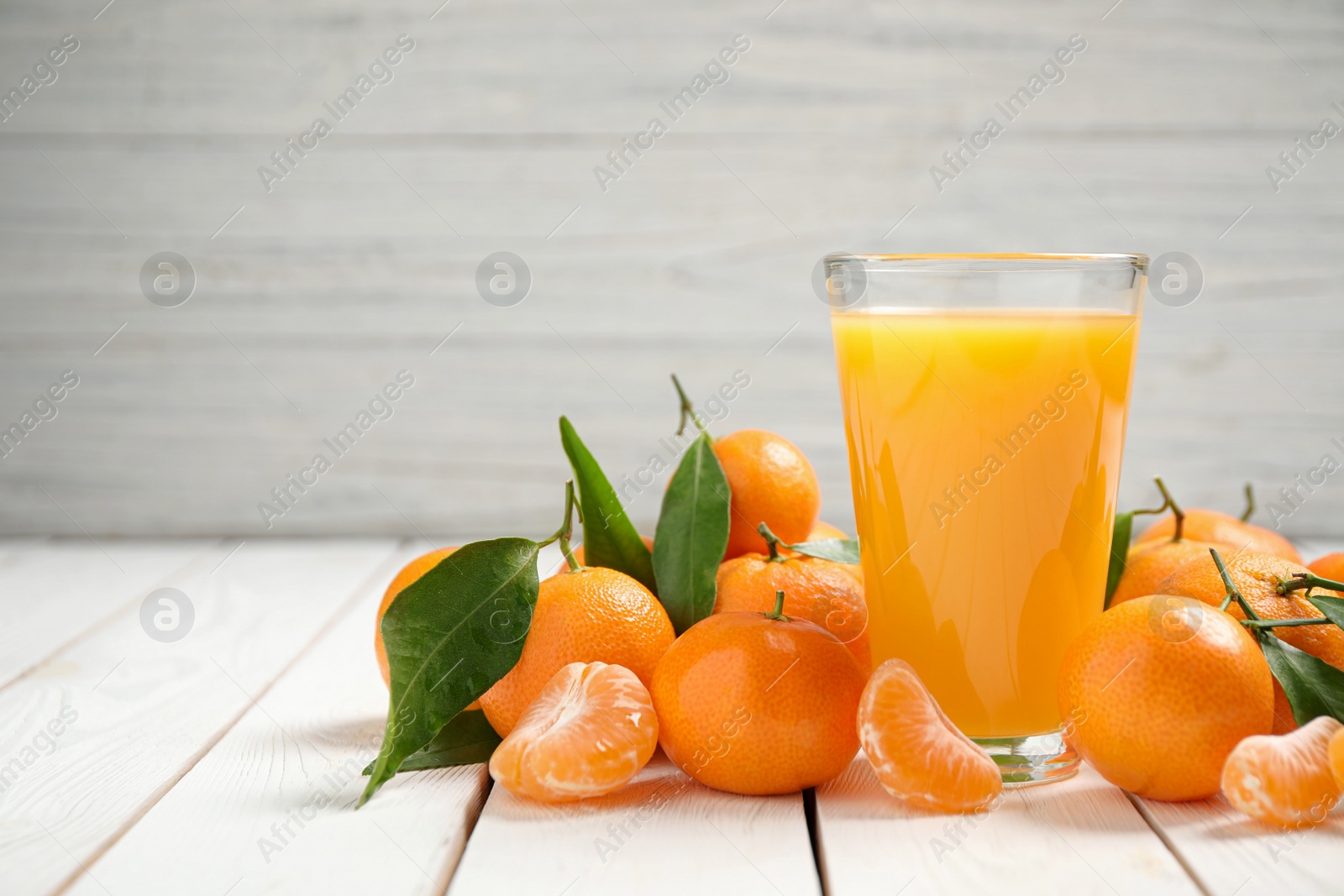 Photo of Glass of fresh tangerine juice and fruits on white wooden table