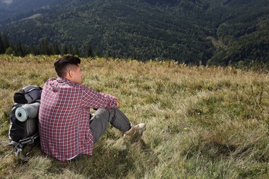 Photo of Tourist with backpack sitting on ground and enjoying landscape in mountains, back view