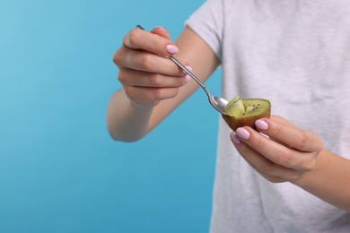Photo of Woman eating kiwi with spoon on light blue background, closeup. Space for text