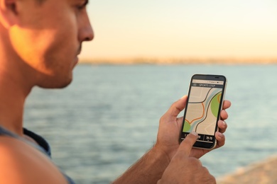 Photo of Man using fitness app on smartphone near river at sunset, closeup