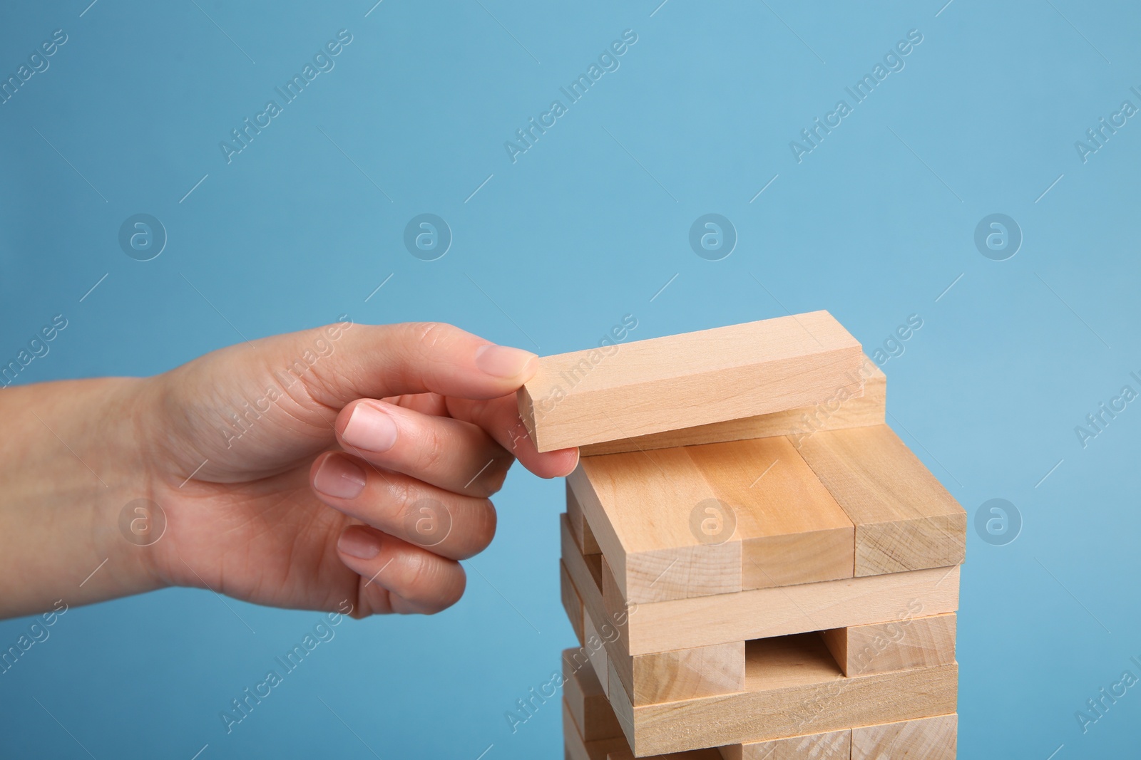 Photo of Woman playing Jenga on light blue background, closeup