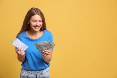 Portrait of happy young woman with lottery ticket and money on yellow background, space for text